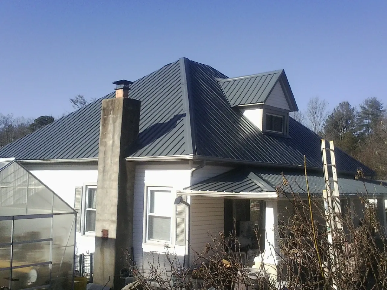 Dark blue standing seam metal roof on a white farmhouse with dormer — Slate & Tile Roof Repair by Roofing Brothers in Oswego