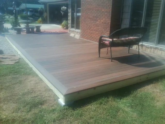 New wood deck and wicker chair beside a brick house in Oswego