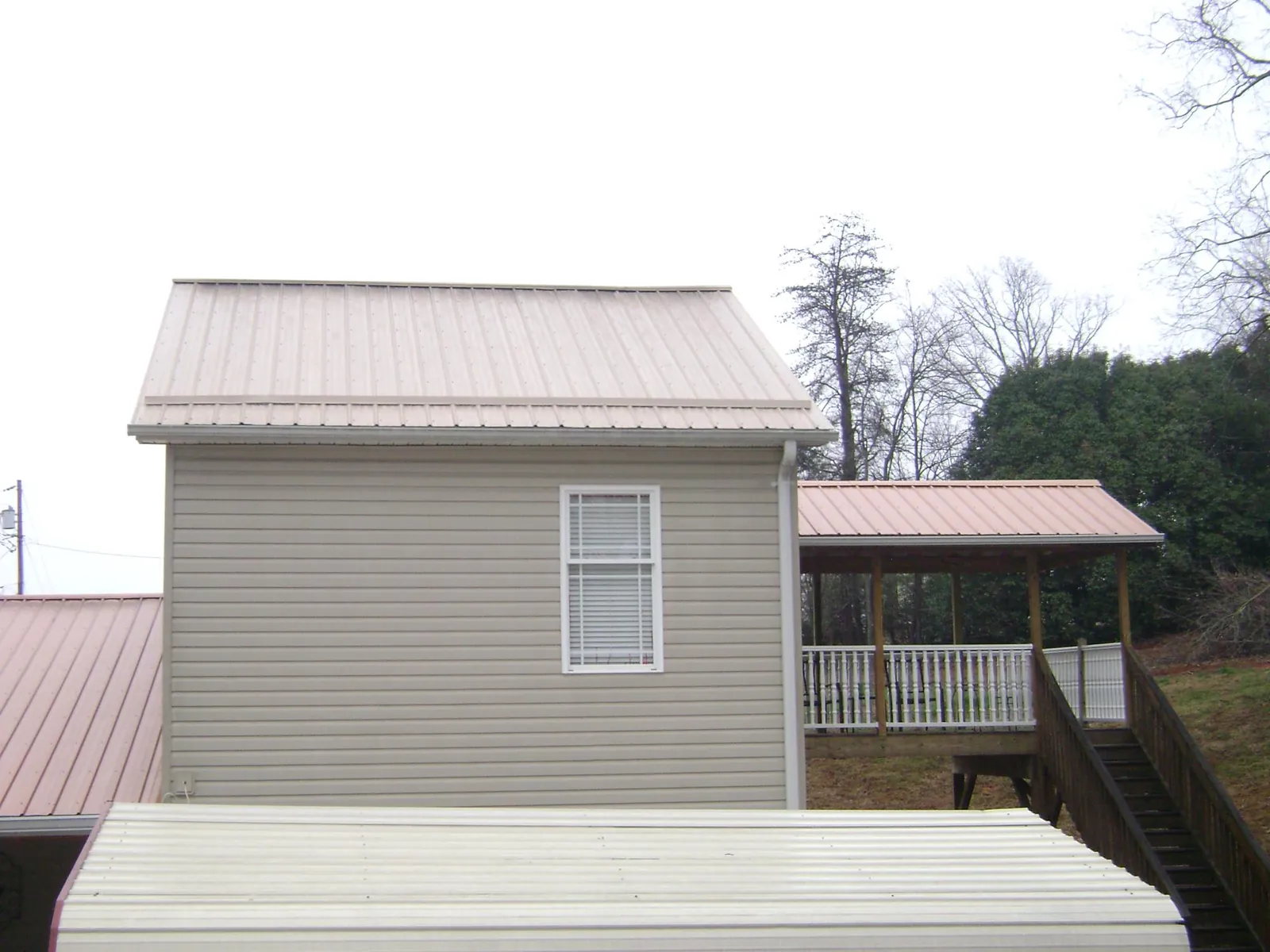 Tan metal roofs on a two story addition and attached porch, from a Roof Replacement job in Oswego